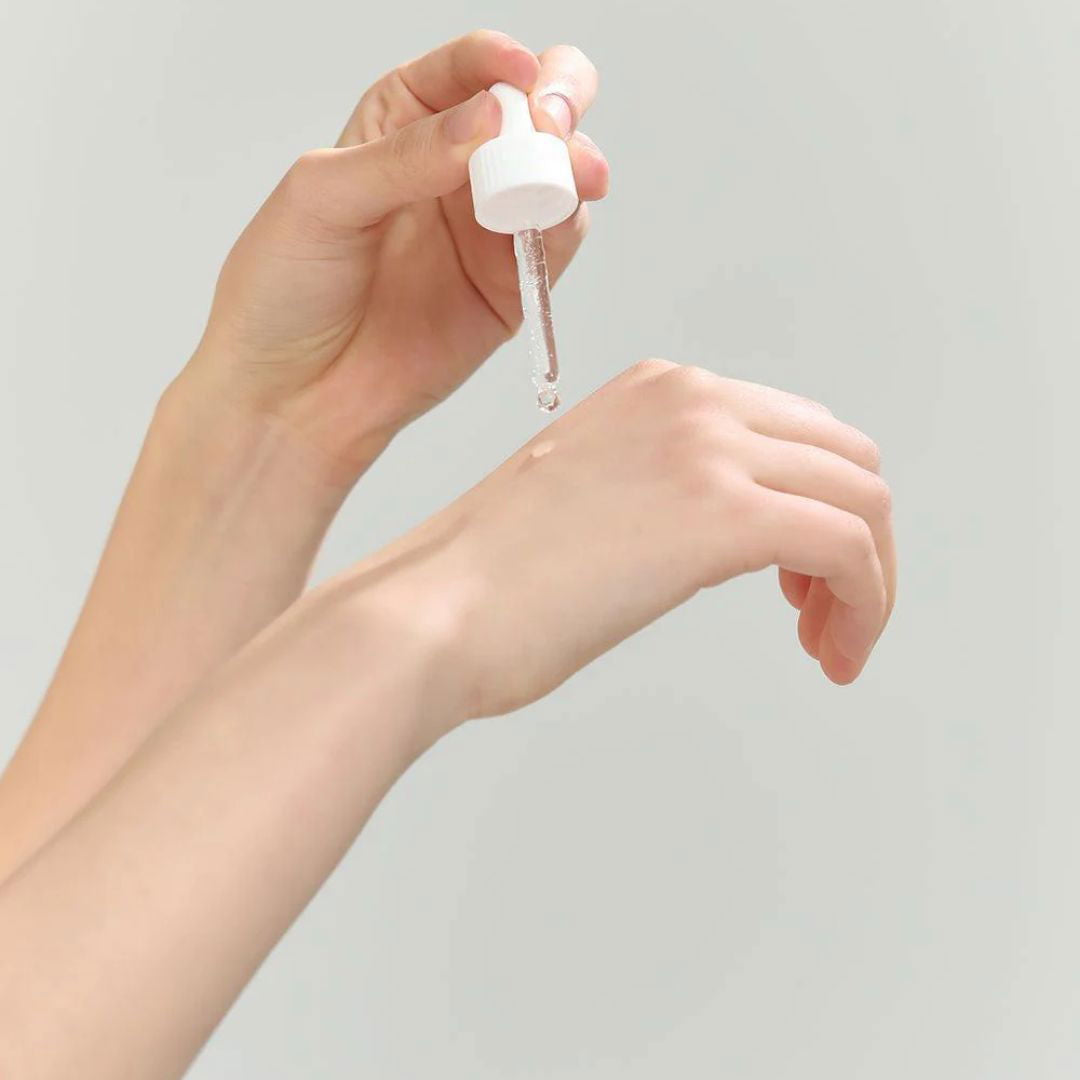 Hand holding a small white dropper bottle with clear liquid against a plain background