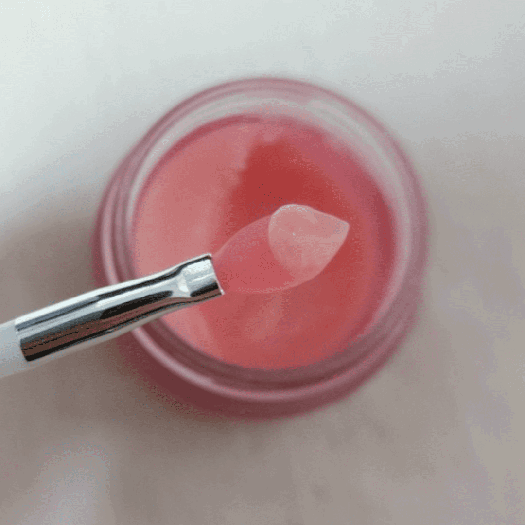 Pink lip balm in a container with a applicator on a light pink background