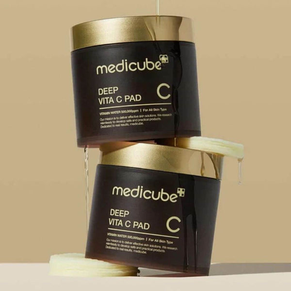 Two Medicube Deep Vita C Pad containers with cream oozing out on a beige background
